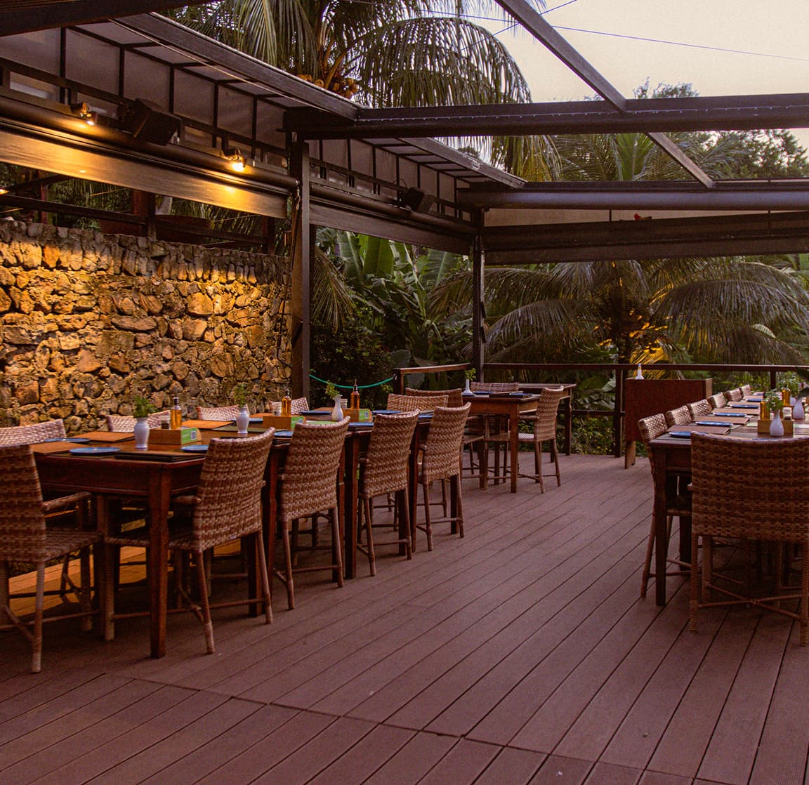 Deck do Restaurante do Vale ao entardecer com mesas postas e parede de pedra vulcânica em Fernando de Noronha